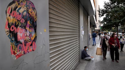 Shoppers pass a masks street vendor sitting on the ground next to a shop that has closed amid the country's economic crisis.