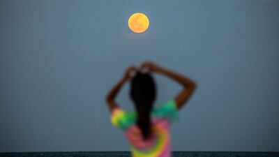 A pink supermoon is seen in the background as people relax on the beach in Miami Beach, US, on June 24, 2021. Four supermoons will grace the skies in 2022. AFP